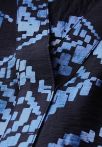 Tessuto nero con un motivo geometrico blu e diverse forme. Cuciture visibili lungo i bordi dell'indumento, texture liscia e colori vivaci.