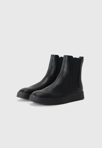 Botas de tobillo negras hechas de cuero texturizado, con paneles laterales elásticos, punta redondeada y suela de goma gruesa.