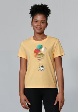 Gele katoenen t-shirt met een astronautenafbeelding die kleurrijke ballonplaneten vasthoudt. Ronde hals, korte mouwen en een relaxte pasvorm.