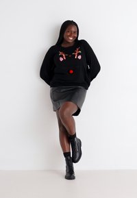 Schwarzer Pullover mit Rentierdesign, roten Pom-Pom-Akzenten, kombiniert mit einem schwarzen Lederrock und schwarzen Schnürstiefeln. Glatte Texturen.