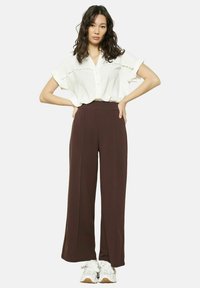 Chemisier blanc boutonné avec des manches courtes, associé à un pantalon marron taille haute et ample, et des baskets blanches. Tissu lisse avec des détails subtils.