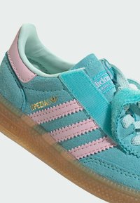 Zamszowy turkusowy tenisówka z różowymi paskami, jasnoróżową łatą na pięcie, złotym napisem "SPEZIAL", przezroczystą brązową podeszwą oraz paskiem na rzep.