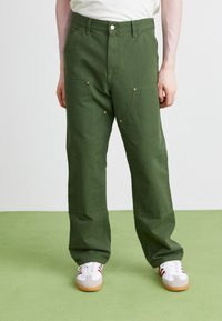 Groene katoenen broek met een relaxte pasvorm, voorzien van voorzakken, gouden hardware accenten en een kenmerkend gestikt ontwerp, gecombineerd met witte sneakers.