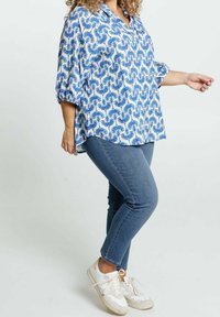 Camicia a maniche corte a righe blu e bianche, abbinata a jeans blu e sneakers bianche, che mostrano un fit rilassato e un design casual.