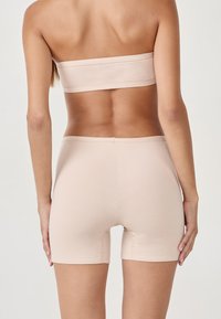 Top bandeau beige sans coutures et shorts assortis à mi-cuisse, fabriqués à partir d'un tissu lisse, avec une coupe ajustée et des coutures minimales.