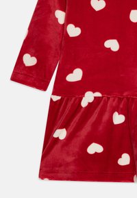 Robe en velours rouge avec des manches longues, ornée de motifs de cœurs blancs et d'une jupe froncée. Texture douce, col rond et poignets sans couture.
