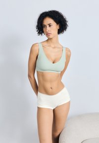 Lys grønn, sømløs bh med dyp V-hals-design og brede stropper; parret med kremfargede boyshorts med blondedetaljer.