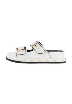 Witte slippers met twee verstelbare banden met gouden gespen, een zwarte rand aan de zool en gouden studs langs de plateauzool.