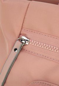 Dettaglio di una borsa in nylon rosa con una superficie liscia, chiusura con zip in metallo argentato e accenti grigio chiaro a contrasto sulla tracolla.
