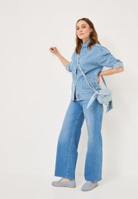 Lichtblauwe denimjack met opgerolde mouwen, gecombineerd met wijde lichtblauwe jeans. Geaccentueerd met een kleine lichtblauwe tas met een sjaal detail.