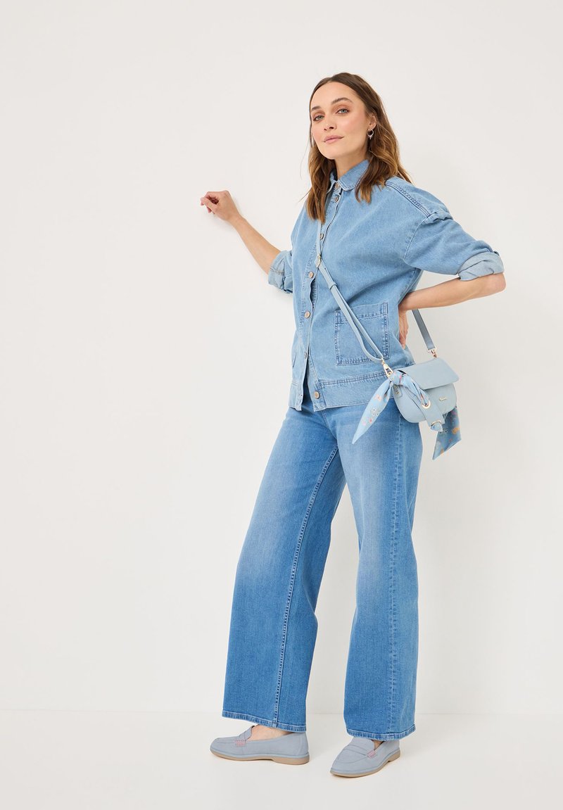 Lichtblauwe denimjack met opgerolde mouwen, gecombineerd met wijde lichtblauwe jeans. Geaccentueerd met een kleine lichtblauwe tas met een sjaal detail.