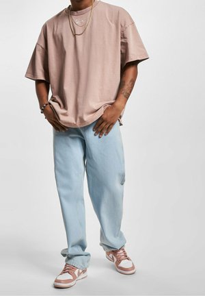 Übergrößen, hellrosa Baumwoll-T-Shirt mit lockerer Passform und Rundhalsausschnitt sowie gesticktem Logo; kombiniert mit hellblauen Jeans und rosa Sneakers.