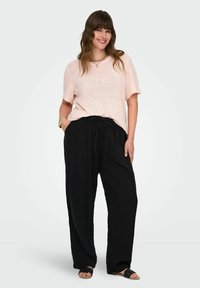 Šviesiai rožinė trumpomis rankovėmis megzta palaidinė derinama su juodomis kelnių su raišteliu ir juodais sandalais. Medžiaga turi tekstūruotą paviršių.