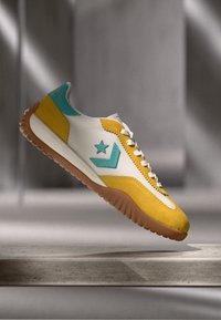 Lace-up sneaker featuring a white leather upper with yellow and turquoise accents, a textured gum sole, and a star logo on the side.