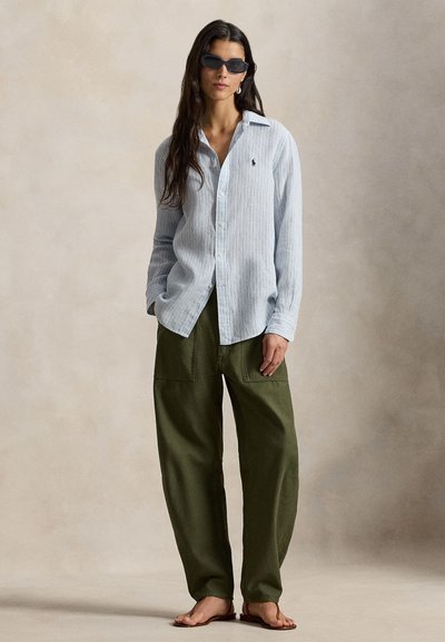 Φωτεινό γαλάζιο πουκάμισο με κάθετες ρίγες και κουμπιά, με μακριά μανίκια, σε συνδυασμό με παντελόνι cargo σε χακί αποχρώσεις και φαρδιά γραμμή. Η εμφάνιση ολοκληρώνεται με κομψά μαύρα γυαλιά ηλίου.