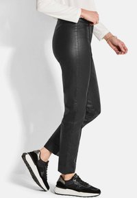 Pantalons noirs en cuir synthétique avec une coupe ajustée et une longueur courte, associés à des baskets noires avec des accents métalliques sur un fond clair.