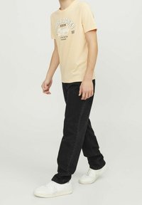 Ljus persikofärgad t-shirt med kort ärm och svart grafisk tryck; matchad med löst sittande svarta jeans och vita sneakers.