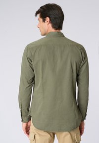 Camicia a maniche lunghe di color verde oliva con colletto con bottoni, orlo dritto e polsini regolabili; realizzata in un tessuto leggero e testurizzato.