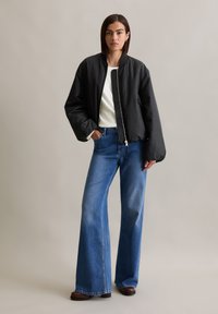 Zwarte bomberjack met een rits, witte shirt eronder, brede blauwe jeans en bruine laarzen. Eenvoudig ontwerp met een casual pasvorm en zachte textuur.