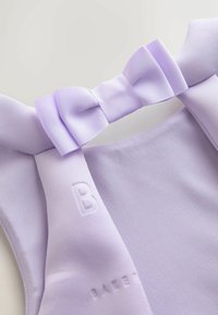 Lilla-farvet beklædningsgenstand med en ribbet sløjfedetalje og præget bogstav "B" på blødt struktureret stof.