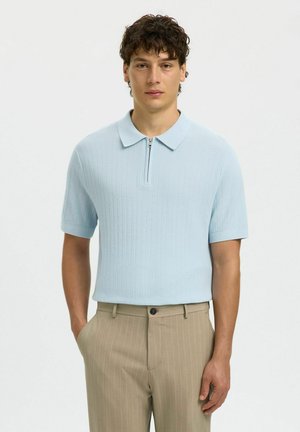 Lyseblå kortærmet poloshirt med zip-lukning og tekstureret strikdesign, kombineret med beige stribede bukser.