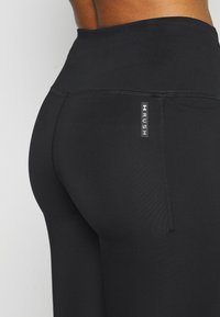 Svarta högmidjade tights gjorda av stretchigt material, med en subtil glans, platta sömmar och en liten logotags nära midjan.