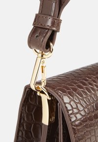 Sac à main en cuir embossé crocodile marron avec une finition brillante, doté de matériel en or et d'une bandoulière amovible. La surface texturée ajoute du détail.