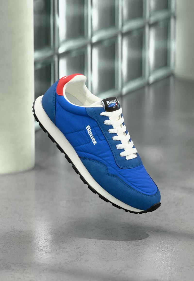 Baskets bleues avec lacets blancs, semelle en caoutchouc, empeigne rembourrée et accent rouge à l'arrière. Logo de la marque "Blauer" affiché sur le côté et la languette.