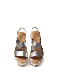 Metallisch zilveren sandalen met kruisbanden en een verstelbare gesp. Natuurlijke leren binnenzool, geweven jute afwerking en een sleehak.