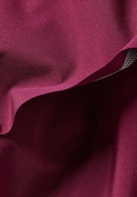 Primo piano di un tessuto drappeggiato con una superficie liscia di un profondo magenta, che mostra un bordo piegato che rivela una fodera bianca con pois neri.