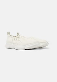 Sneakers bianchi senza lacci con una parte superiore in tessuto morbido, rifiniture elastiche arricciate e una suola ammortizzata spessa. Piccole linguette sul retro.