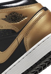 Černé a zlaté tenisky s lesklým povrchem, které mají bílou mezipodešev, texturovanou černou podrážku a embosované logo "Air Jordan".