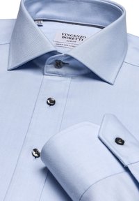 Schmal geschnittenes, hellblaues Hemd aus weichem Stoff. Verfügt über einen Kentkragen, schwarze Knöpfe und ein sauberes Manschettendesign. Etikett im Kragen sichtbar.