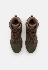 Botas de senderismo marrones y verdes con caña alta, de material de ante, forro de forro polar marrón y cordones marrones y naranjas, con ojales de metal y suelas de goma.