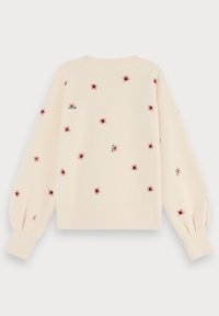 Sweatshirt saumon clair avec de longues manches bouffantes. Présente des motifs d'araignées rouges dispersés et de petits détails en texte noir. Tissu doux, col rond.