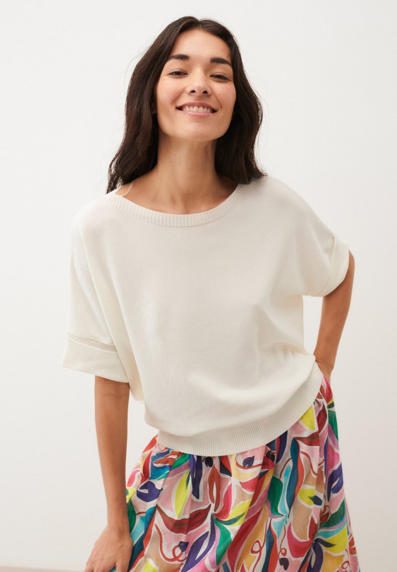 White short-sleeve sweater with ribbed collar, paired with a colorful, patterned skirt featuring swirls in pink, green, and blue hues.