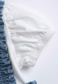 Denim top with puffed white cotton sleeves. Ruffled texture along the denim edge, soft fabric with elasticized cuffs.