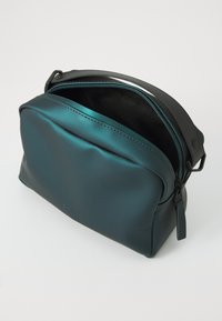 Borsa impermeabile color teal in materiale liscio, forma rettangolare, con una cerniera e rivestimento neri. Presenta un sottile dettaglio del logo sulla parte anteriore.