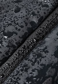 Tela negra resistente al agua con una superficie texturizada, que presenta gotas y un detalle de cremallera en contraste a lo largo de uno de los bordes.