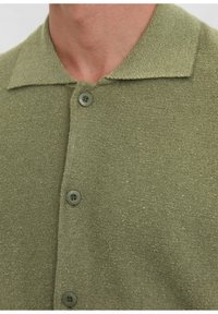 Olive green knit polo shirt with a textured fabric, spread collar, and three matching buttons on the placket.