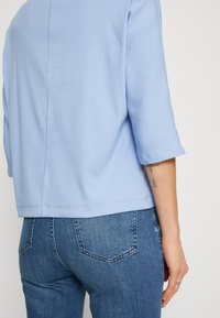 Maglietta a coste azzurro chiaro con maniche a tre quarti, caratterizzata da un dettaglio della cucitura sul retro. Abbinata a jeans in denim blu scuro aderenti.