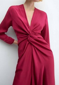 Abito a portafoglio fucsia con maniche lunghe, caratterizzato da un profondo scollo a V e dettagli al torace attorcigliati. Tessuto satinato liscio con drappeggio.