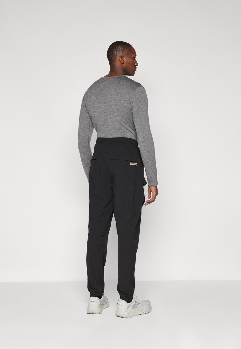 Czarne zwężane spodnie z wieloma kieszeniami i elastycznym pasem, zestawione z dopasowaną szaro-skalową bluzką z długim rękawem. Lekka, codzienna konstrukcja.