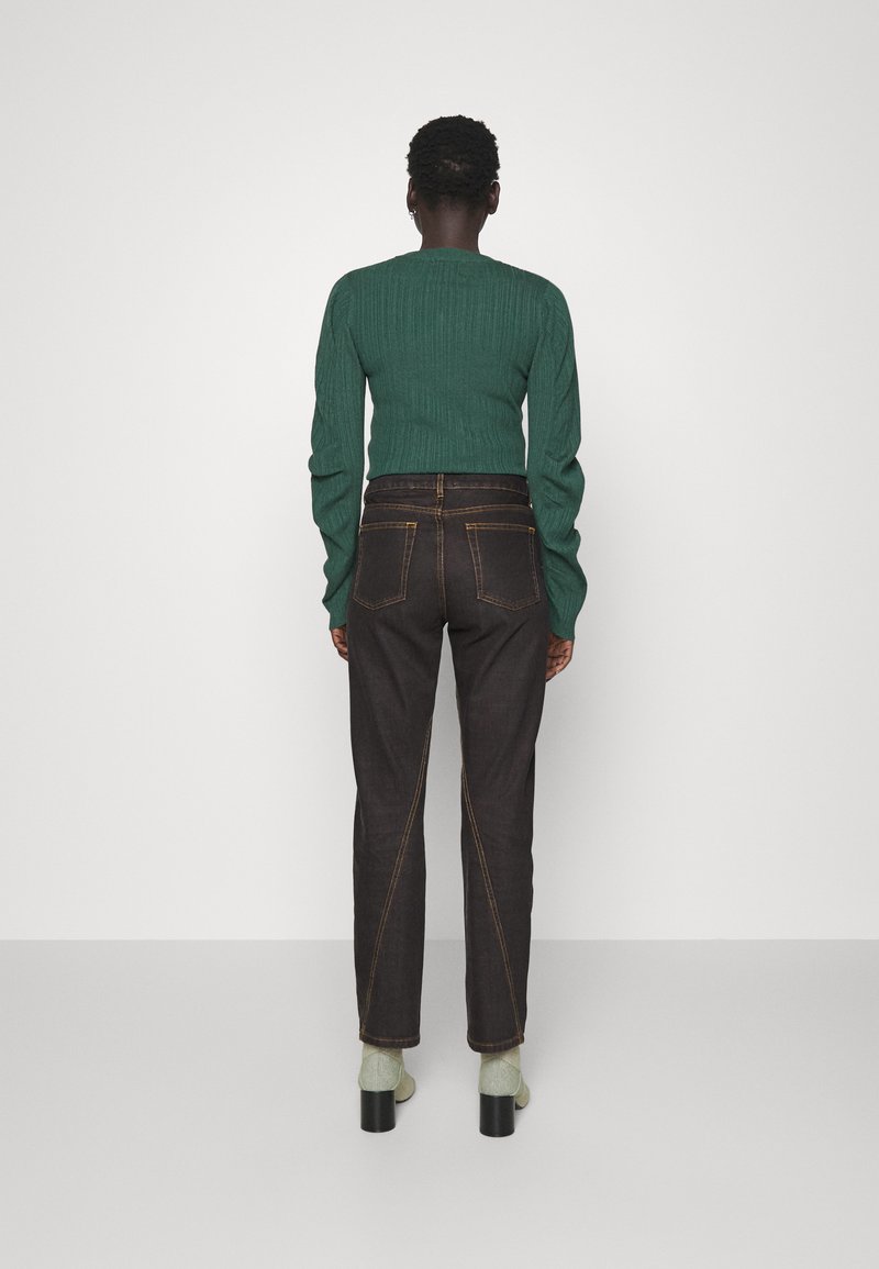 Dunkelblaue Jeans mit Doppelnaht und modernem Schnitt, kombiniert mit einem strukturierten grünen Rippensweater und grünen Knöchelsocken.