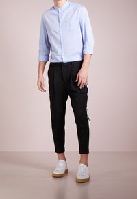 Lichtblauw collobloes, zwarte tapered broek met een witte zijkantstreep, en witte sneakers met beige zolen. Gladde texturen, casual ontwerp.
