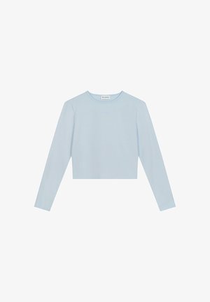 Light blue, long-sleeved crop top made from soft fabric. Features a round neckline and subtle branding on the front. Simple design, no patterns.