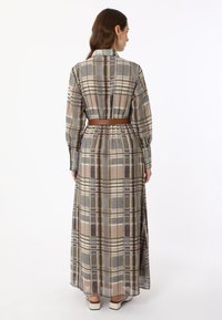 Long plaid dress in soft fabric. Features a collar, long sleeves, and a brown belt at the waist. Color palette includes beige, gray, and green.