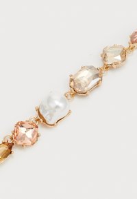 Guldtonet armbånd med uregelmæssigt formede krystaller i pink, ferskenfarvet og klare nuancer samt en stor hvid perle som accent.