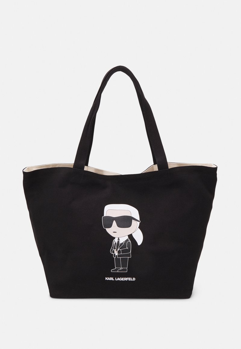 Bolsa de tote negra de lienzo que presenta un personaje de dibujos animados con gafas de sol, con un interior crema y texto "KARL LAGERFELD" en la parte inferior.