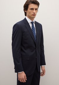 Dark navy suit with thin vertical stripes, single-breasted design, two-button closure, and notch lapels, paired with a white shirt and striped tie.